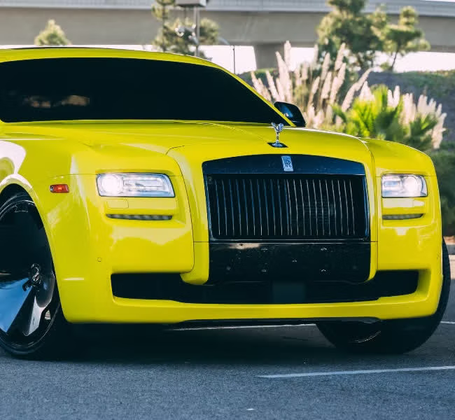 Close-up of the grille and Spirit of Ecstasy on a bright yellow Rolls-Royce Ghost wrapped by Monarch